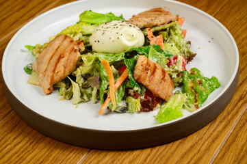 Caesar salad with croutons, quail eggs, cherry tomatoes and grilled chicken in wooden table