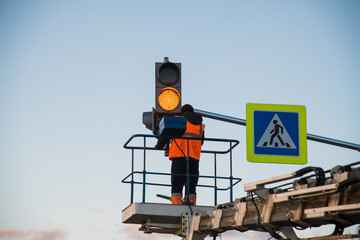 Worker on the lift sets and adjusts the traffic light at the pedestrian crossing