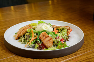 Caesar salad with croutons, quail eggs, cherry tomatoes and grilled chicken in wooden table