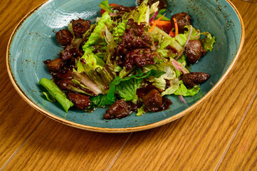 Salad with fried mushrooms, tomatoes and lettuce on a wooden table