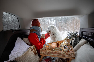 Woman with her dog have a picnic in car trunk in winter forest