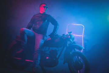Motor biker in the neon lights on the old brick wall background.