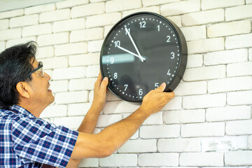Asian technical engineer installing the clock on the wall in the office