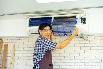 Asian technical engineer maintenance changing filter from air conditioner in the office 