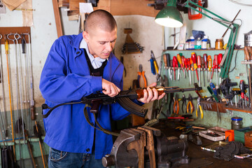 Concentrated skilled craftsman of weapons workshop disassembling AK assault rifle for repair .