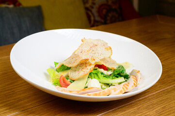 Caesar salad with croutons, quail eggs, cherry tomatoes and grilled chicken in wooden table