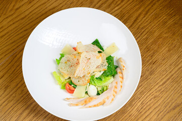 Caesar salad with croutons, quail eggs, cherry tomatoes and grilled chicken in wooden table
