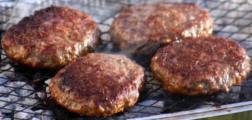 Close up of juicy beef burgers cooking on a cheap disposable barbecue