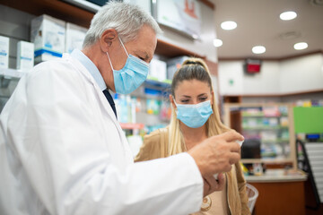 Pharmacist suggesting a product to a customer while wearing a coronavirus mask