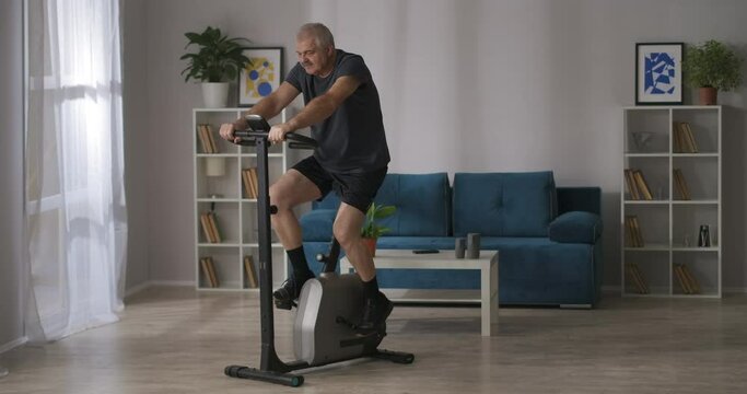 fitness at home, middle-aged man is training on exercise bike in living room, cardio workout