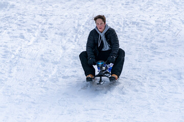 Fototapeta na wymiar A teenage boy races a snow bike sled down a snowy run in the mountains.