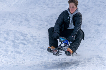 A teenage boy rides catches some air on a snow bike sled on a snowy run in the mountains.
