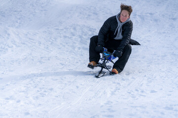 Fototapeta na wymiar A teen boy leans into a turn on with a snow bike sled on a downhill run on a snowy slope.