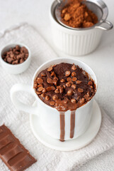 Chocolate mug cake in white cup with chocolate drops and coca powder
