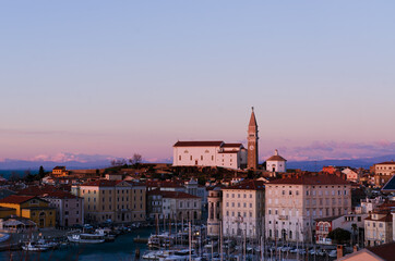 Red roofs of the historical center of old town Piran with main church against the sunset sky and...