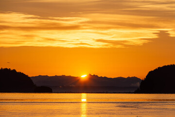 Dramatic sun rising between two hills with water in the foreground.