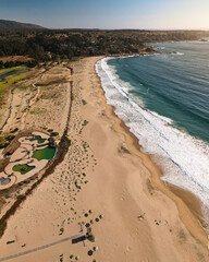 Vista aérea de la Playa Grande de Quintay con el fondo de bosques y el sol iluminando la arena en un día soleado