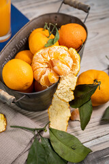 Several ripe tangerines with leaves in a container lie on a white table against a light background. Rustic style copyspace.