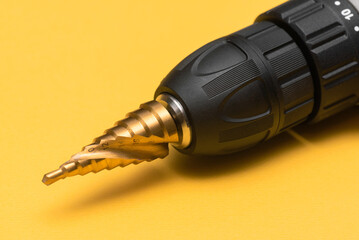 Step conical drill bit on the yellow background close up.
