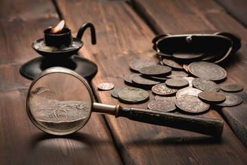 Old ancient coins and magnifying glass on the wooden desk table close up background.