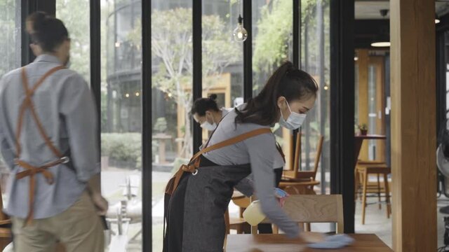 restaurant workers wearing a protective face mask to prevent coronavirus spread and cleaning table before the open. slow motion