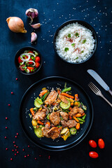 Fried pork steaks and mic of vegetables served on black wooden table
