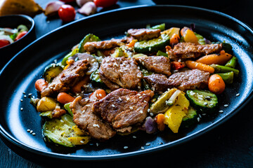 Fried pork steaks and mic of vegetables served on black wooden table
