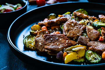 Fried pork steaks and mic of vegetables served on black wooden table

