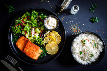 Fried salmon steak with mix of vegetables served on black plate on wooden table
