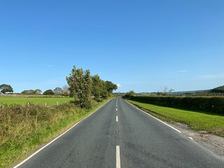 Looking along the, B6165, with trees and fields, set against a vivid blue sky in, Hartwith cum Winsley, Harrogate, UK