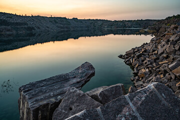 Old flooded stone quarry surrounded by stone waste from a mine work against a beautiful night sky