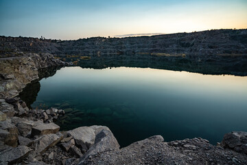 Fototapeta na wymiar Old flooded stone quarry surrounded by stone waste from a mine work against a beautiful night sky