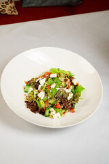 Vegetable vegetarian salad with tomatoes, peppers and onions on white table.
