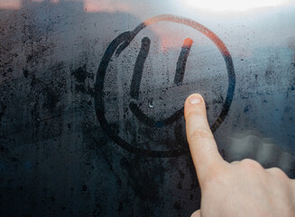 Hand draws a smiley face on a foggy window