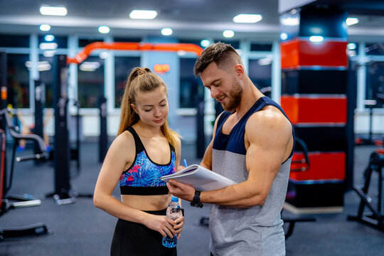 Beautiful young woman with her personal trainer at the gym discuss her progress on a clipboard held by the man. Healthy lifestyle