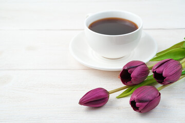 Fototapeta na wymiar Festive background with tulips and a white coffee cup on a light wooden background. Side view, with space to copy. Concept of March 8, spring.