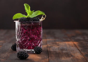 Glass of summer cocktail with blackberry with ice cubes and mint on wooden background with berries....