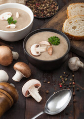 Ceramic bowl plates of creamy chestnut champignon mushroom soup with spoon, pepper and kitchen cloth on dark wooden  background.