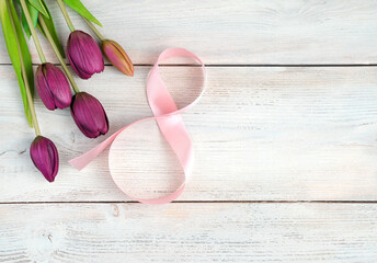 Obraz na płótnie Canvas Figure 8 of ribbon and purple tulips on a light wooden background. Top view, with space to copy. Concept of festive backgrounds, March 8.
