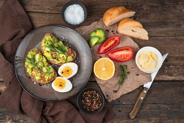 Lunch with toast with guacamole and rosemary, boiled eggs, tomatoes and lemon on a wooden background. Top view, with space to copy. The concept of proper nutrition.