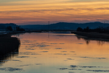 Obraz premium Dusk at Gota river in western Sweden. Orange sky is reflecting in the calm water and ice sheets are floating in the river