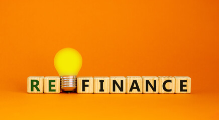 Refinance symbol. Wooden cubes with word 'refinance'. Yellow light bulb. Beautiful orange background. Business and refinance concept. Copy space.