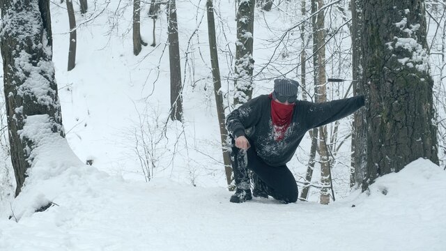 Man in red bandana and black, round glasses using two knives climbs snow covered mountain. Then he sticks the knife into tree and rests
