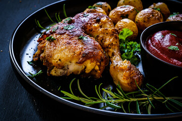 Barbecue chicken drumsticks with baked potatoes on black wooden table