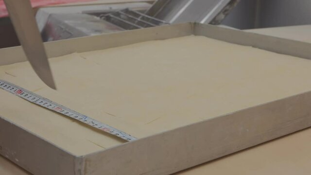 the baker marks the dough on the baklava portions with a ruler. Marking the dough into pieces of baklava using a ruler and a knife. Close-up.