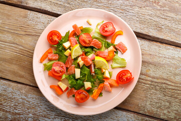Salad with salmon and cherry tomatoes and green salad in a plate on a wooden table.