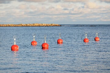 Orange mooring buoys in the new yacht harbor (marina), close-up. Water surface texture. A view from the pier. Work safety, special equipment, sailing, cruise, sport, recreation