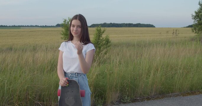 Young, attractive girl posing with skateboard and flirting at camera out of city