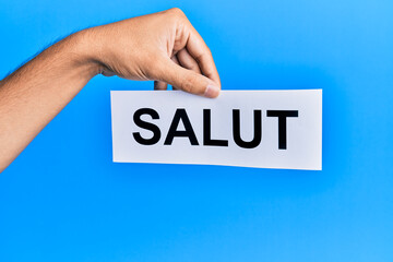 Hand of hispanic man holding salut word paper over isolated blue background.