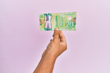 Hispanic hand holding 20 canadian dollars banknote over isolated pink background.